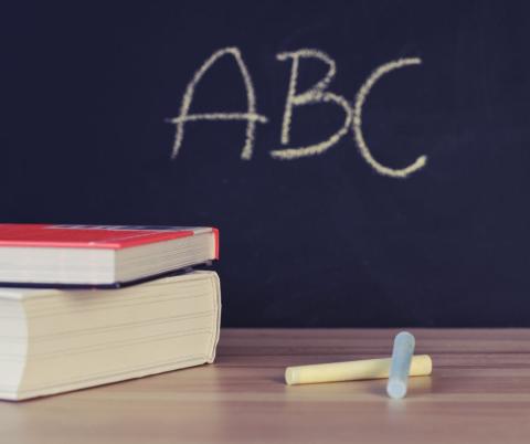 due libri su un tavolo con sfondo lavagna nera con scritta A B C 